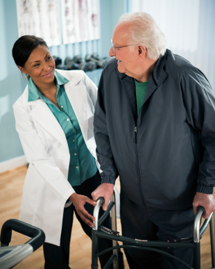 Active senior male walking with walker with physical therapist.